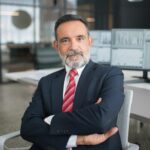 Professional businessman sitting confidently in a modern office with multiple screens displaying data.